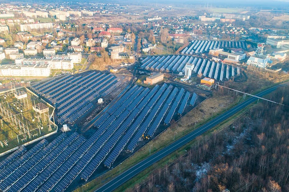 Lotnicze ujęcie gminnej farmy fotowoltaicznej otoczonej zabudową mieszkalną – wizualizacja lokalnej niezależności energetycznej.